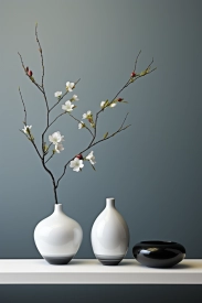 A white vase with a branch with flowers in it