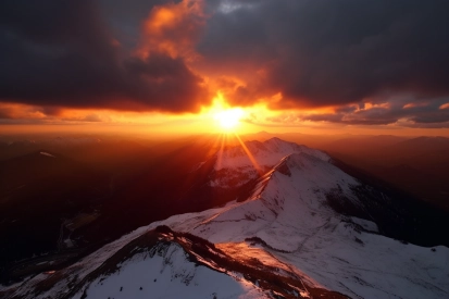 A sun shining through clouds over a snowy mountain