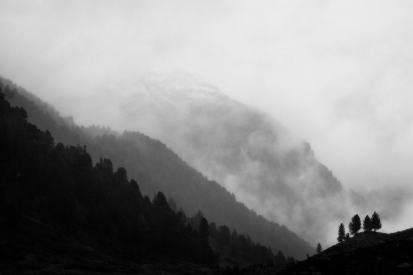 Black and white image of mountains with fog and trees